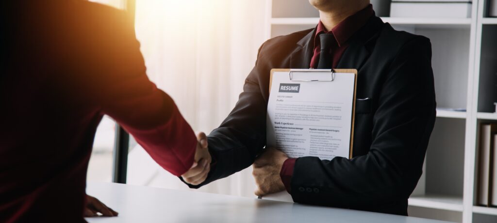 A newly hired job applicant holding a resume shaking hands with a recruiter.