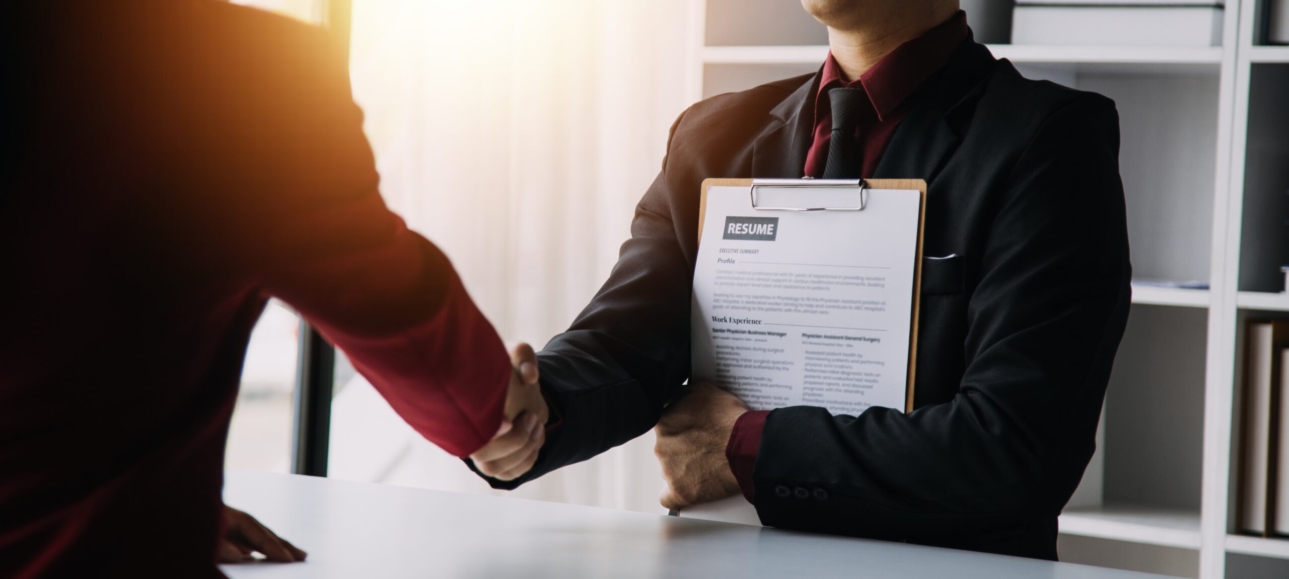 A newly hired job applicant holding a resume shaking hands with a recruiter.